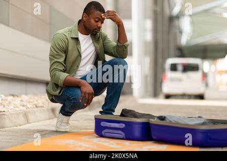 Unhappy Black Male Tourist Having Problem With Luggage At Airport Stock Photo