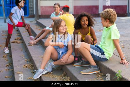 Happy tweenagers friends sitting on steps outdoors and chatting Stock Photo