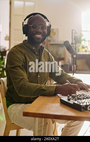 Young successful African American male host in headphones looking at camera while sitting by desk and making plan of speculation Stock Photo