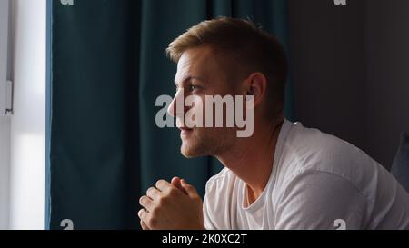 A young man watches a movie and eats roasted corn while sitting in the living room on the couch in his home Stock Photo