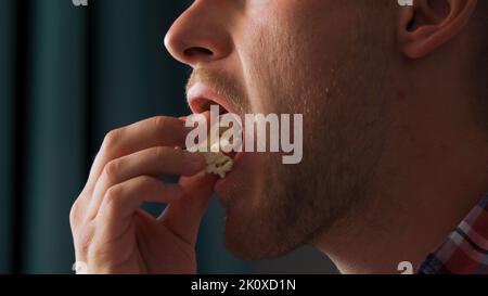 A young man watches a movie and eats roasted corn while sitting in the living room on the couch in his home  Stock Photo