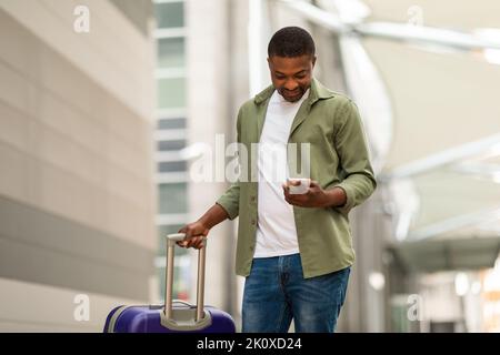 Happy Black Man Using Phone With Travel Application At Airport Stock Photo