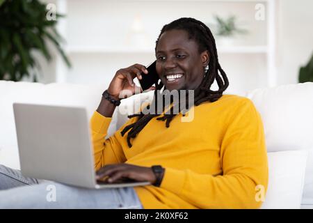 Happy Young African American Man Using Laptop And Talking On Mobile Phone Stock Photo