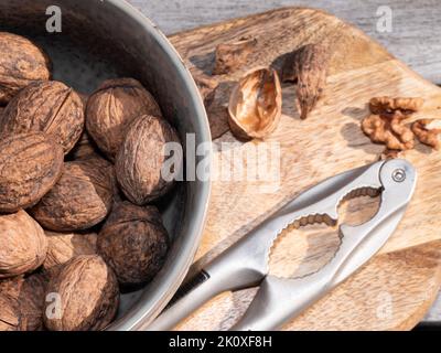 Close up of walnuts in a bowl with walnut shells in the background, and a nutcracker Stock Photo