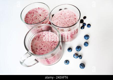 Three glasses with blueberry smoothie, berries on white background. Stock Photo