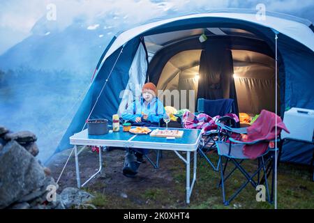 Kids, sitting around campfire at night, enjoying wild camping, family vacation in Norway Stock Photo