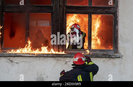 Firefighter hero carrying baby girl out from burning building area from fire incident. Rescue people from dangerous place Stock Photo