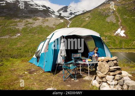 Kids, sitting in front of a piched tent in nature, eating, enjoying wild camping. Family vacation Stock Photo