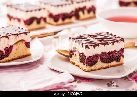 German cake Donauwelle (Danube waves) - vanilla and chocolate sponge cake with sour cherries, vanilla buttercream and chocolate icing with cup of tea Stock Photo