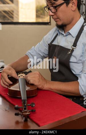 Vertical portrait of a hispanic artisan fixing the bridge of a violin in a workshop Stock Photo