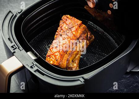 Cooking crispy pork belly in airfryer. Fast and easy crispy food cooking with little or no fat by circulating hot air inside the basket Stock Photo