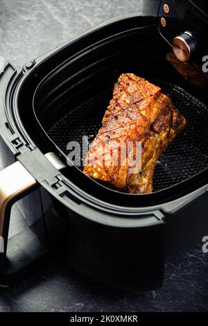 Cooking crispy pork belly in airfryer. Fast and easy crispy food cooking with little or no fat by circulating hot air inside the basket Stock Photo