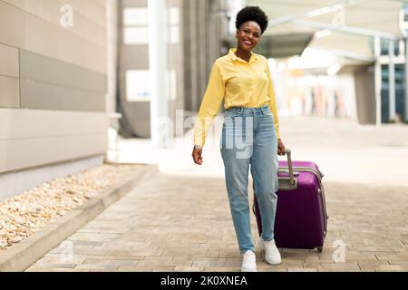 Joyful Black Female Posing With Suitcase Walking At Airport Outdoors Stock Photo