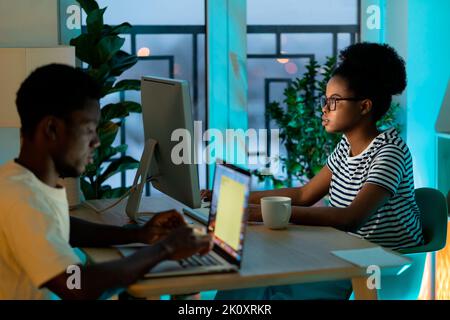 African American couple works on devices typing information about project sitting at table together Stock Photo