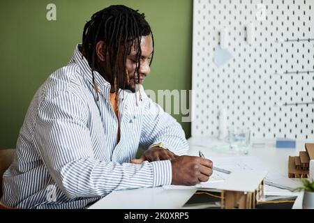 African man sitting at his workplace and making plans for construction project Stock Photo