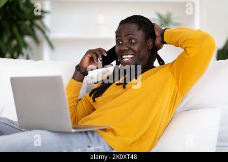 Excited Happy Black Man Talking On Cellphone And Using Laptop At Home Stock Photo