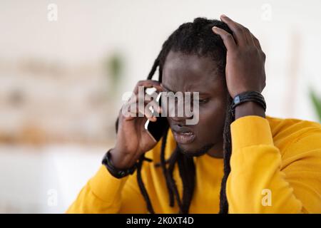 Confused Young Black Guy Talking On Cellphone And Touching Head Stock Photo