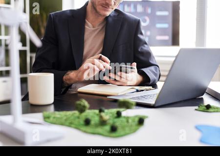 Close-up of young businessman sitting at his workplace with laptop and using mobile phone in his work Stock Photo