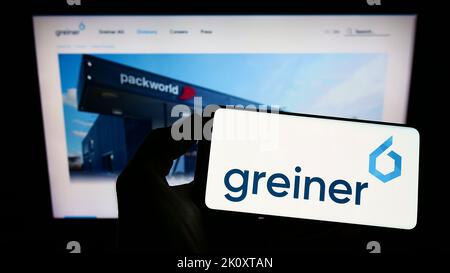 Person holding smartphone with logo of Austrian plastics company Greiner AG on screen in front of website. Focus on phone display. Stock Photo