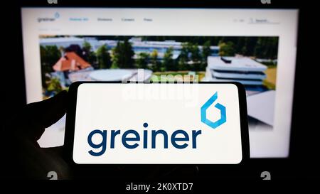 Person holding cellphone with logo of Austrian plastics company Greiner AG on screen in front of business webpage. Focus on phone display. Stock Photo