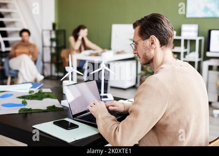 Young businessman in eyeglasses concentrating on his online work on laptop at table at office Stock Photo