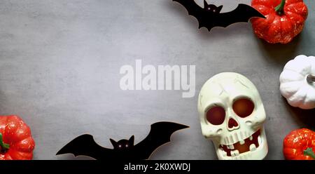 Holidays, decoration and party concept -scull, black bats and pumpkins halloween over gray background. Stock Photo