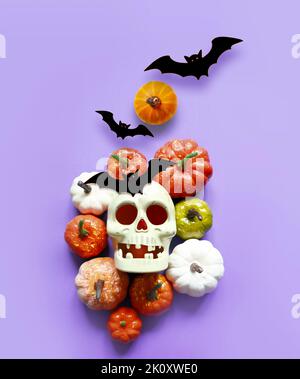 Holidays, decoration and party concept -scull, black bats and pumpkins halloween over violet background. Stock Photo