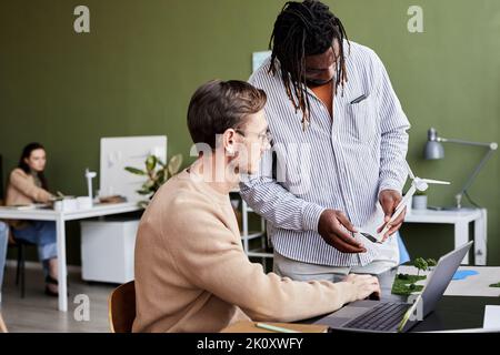 African businessman talking about windmill with his colleague while he working on laptop at office Stock Photo