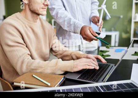 Close-up of businessman sitting at table and working on laptop with his colleague pointing at monitor and discussing online project Stock Photo
