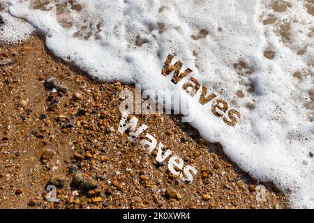 Waves text cut out on both pebble beach and lapping waves  Stock Photo