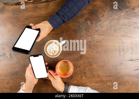 Two smartphone mock up, top view photo of two smartphone mock up. Couple sitting on the wooden table ignoring each other using own mobile phones. Stock Photo