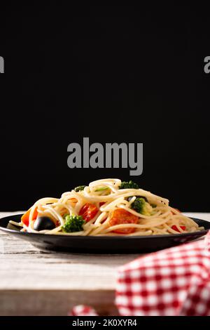 Spaghetti with vegetables(broccoli,tomatoes,peppers) on wooden table and black background Stock Photo