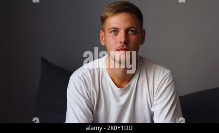 A young man watches a movie and eats roasted corn while sitting in the living room on the couch in his home Stock Photo