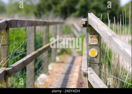 Yellow arrow footpath direction sign on wooden bridge post, countryside service, Hampshire, UK Stock Photo