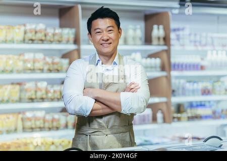 Portrait of successful Asian businessman business owner, man in shop smiling and looking at camera with arms crossed, farmer dairy shop Stock Photo