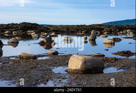 View of boulders above the water in a shallow tidal pool in the early morning light. Stock Photo