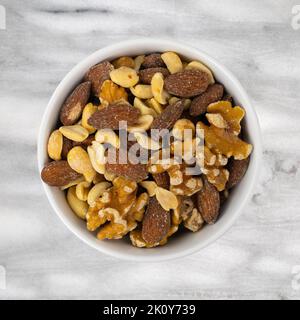 Assorted nuts in a white bowl atop a gray marble tabletop top view. Stock Photo