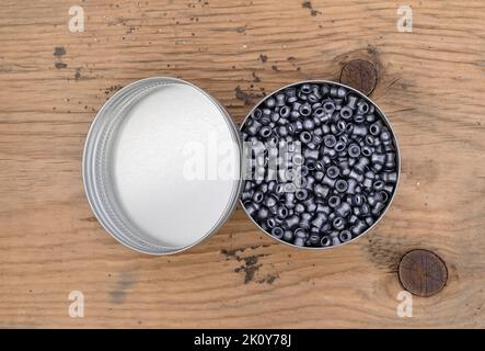 Top close view of an open tin of air gun pellets on a wood board illuminated with natural light. Stock Photo
