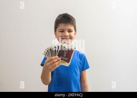 Bauru, Brazil - 09.12.22: Cute happy boy holding Qatar 2022 world cup card packs - FIFA. The cup card album is collected by millions of people all ove Stock Photo
