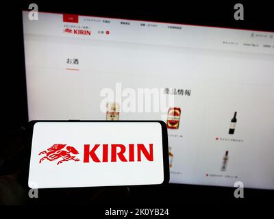 Person holding smartphone with logo of Japanese Kirin Brewery Company Limited on screen in front of website. Focus on phone display. Stock Photo