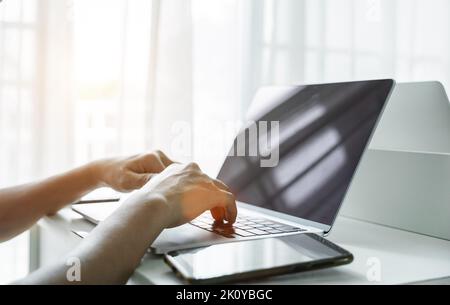 Man's hands using laptop computer with smartphone on white table at home. Online shopping, home work, freelance, online learning concept. Stock Photo