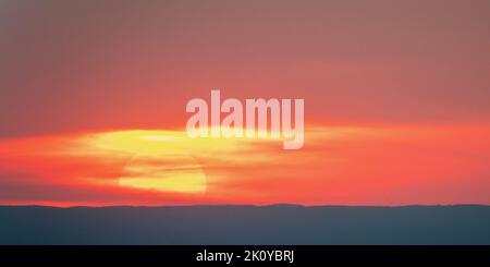Large sun hidden by clouds in the sky at sunset Stock Photo