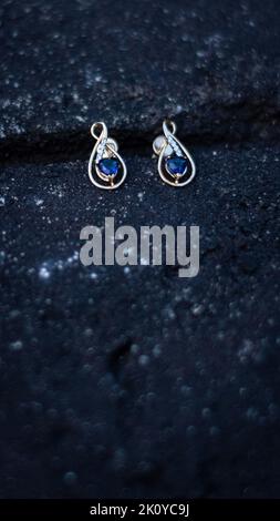A selective focused picture of a pair of gold diamond and sapphire earrings in a black background Stock Photo