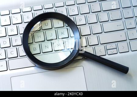 Magnifying glass on laptop keyboard, searching or data security concept Stock Photo