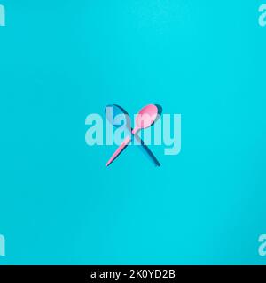 Pink and blue plastic spoons crossed on blue background. Minimal concept. Stock Photo