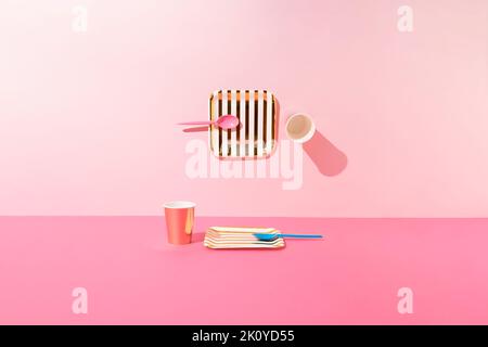 Picnic setup with two gold and white striped paper plates, pink and blue spoons, and rose gold paper cups on pink background. Minimal concept. Stock Photo