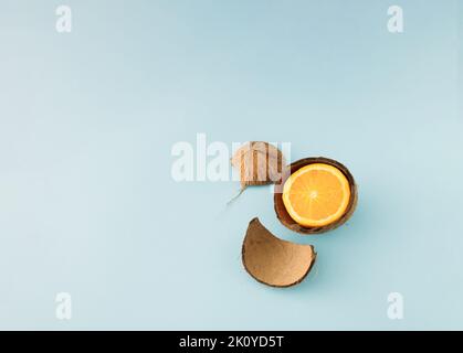 Minimal concept with half an fresh orange inside a broken coconut shell on blue background. Stock Photo