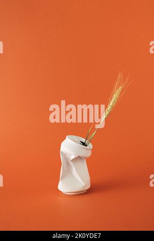 Ear of dried golden wheat in white crumpled beverage can on orange background. Stock Photo