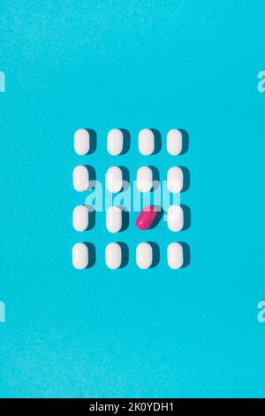 White pills with one tilted pink pill arranged on blue background. Flat lay. Minimal medical concept. Stock Photo