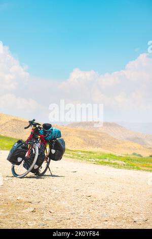 Bicycle standing on countryside gravel road with no person and mountains background. Fully loaded travel around the world set up on two wheels concept Stock Photo